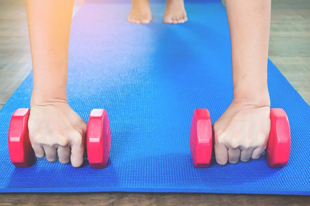 Manos de mujer sosteniendo pesas con pose de tablón completo en estera de yoga de color azul, vista frontal, concepto de estilo de vida saludable con espacio para copiar
 - Foto, Imagen