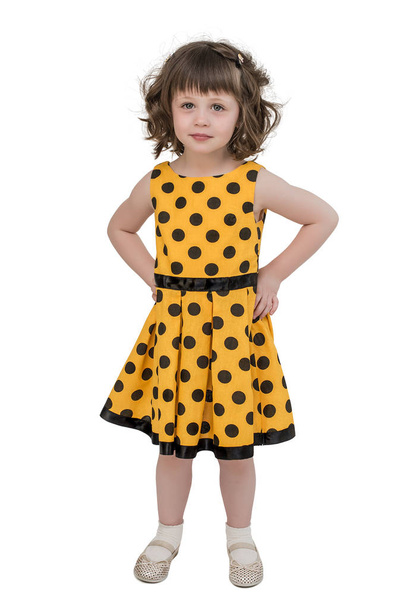 Een charmante meisje in een helder gele jurk, staart naar voren met een belangrijke lucht, handen op haar heupen - Foto, afbeelding