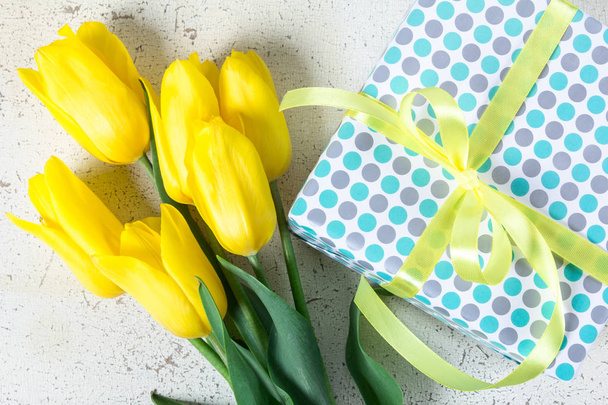Букет желтых тюльпанов и подарочная коробка на белом потрескавшемся фоне
 - Фото, изображение