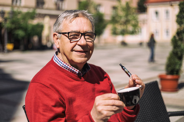 Senior man  drinking coffee and smoking electronic cigarette  - 写真・画像