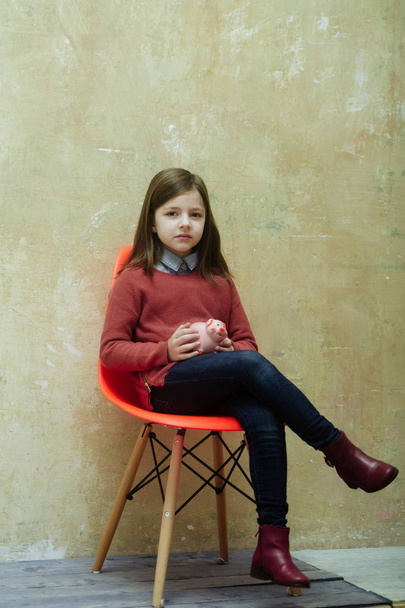 Pretty girl sitting on chair with piggy bank - Фото, зображення