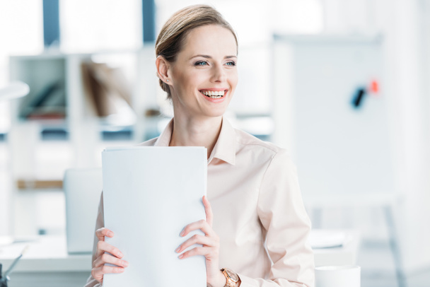 smiling businesswoman holding documents at office - Photo, Image