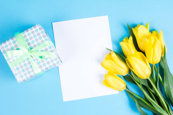 Bouquet of beautiful fresh yellow tulips on blue background and blanc card for text - Foto, imagen