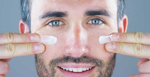A very handsome man smiles and puts the face cream and eye contour anti-wrinkle and anti-aging for the care of his body and knows beauty. Concept: beauty, cream, beauty - Fotoğraf, Görsel
