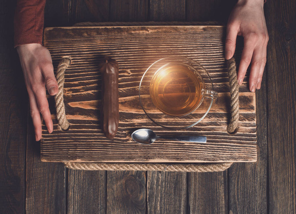 hands with tea and cake on wooden desk - Фото, изображение