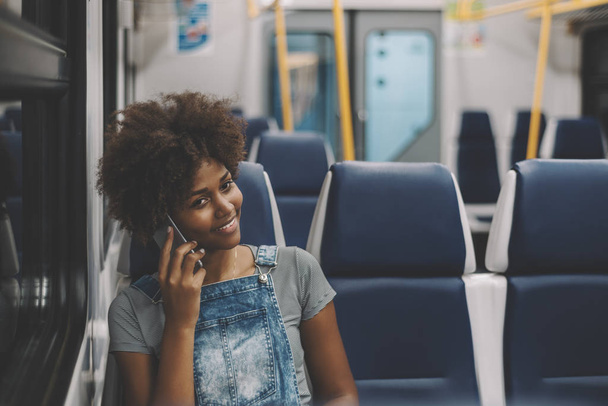 Smiling curly black girl in train using smart phone - Zdjęcie, obraz