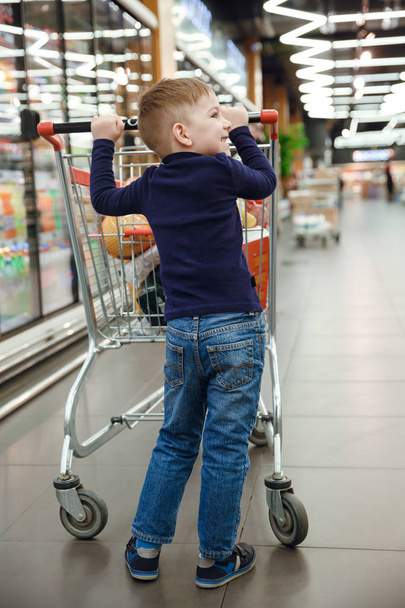 Imagen vertical del niño sonriente con carrito de compras
 - Foto, Imagen