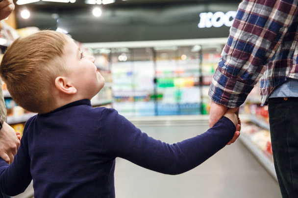 abgeschnittenes Bild von kleinem Sohn, der mit Vater in Supermarkt geht - Foto, Bild