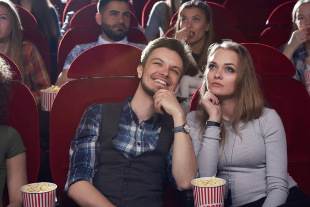 Серьезная женщина и улыбающийся мужчина смотрят кино в современном кино
. - Фото, изображение