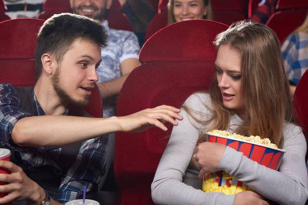Boyfriend pulling hand to popcorn of his greed girlfriend. - Zdjęcie, obraz