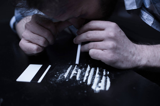 Involved drug addict inhaling cocaine lines in the dark place - Photo, Image