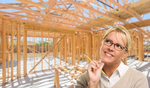 Mujer pensativa con lápiz en el sitio dentro del nuevo marco de construcción del hogar
. - Foto, Imagen