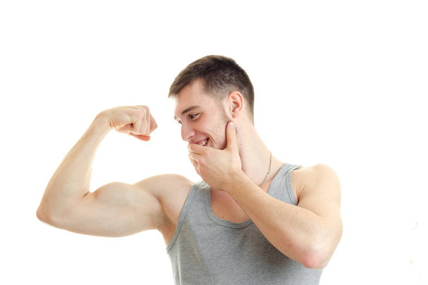 sporty young guy looks on the muscles in the arm and smiling close-up - Foto, Bild