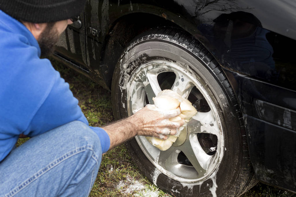 Άνθρωπο πλύσεις ένα σφουγγάρι αυτοκινήτου με ένα σαμπουάν αυτοκινήτου κράμα αλουμινίου. - Φωτογραφία, εικόνα