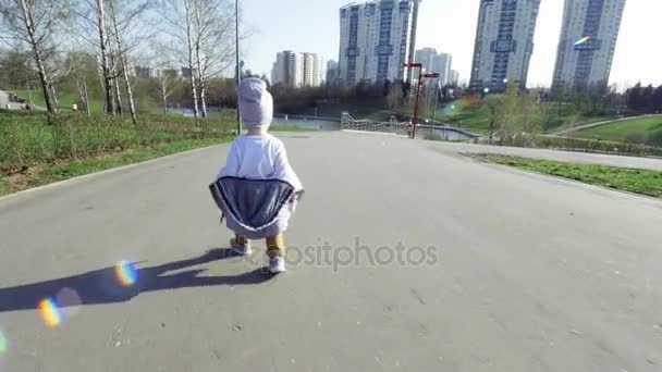 Petit garçon mignon se promène dans le parc par beau temps, faisant un par un pas instable, regarder de l'arrière. L'enfant marche sur une route asphaltée plate
 - Séquence, vidéo