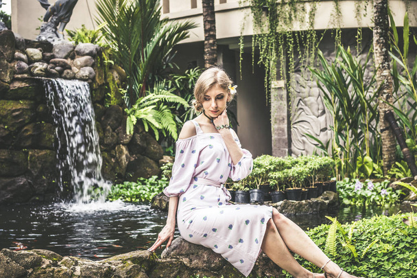 Mujer está posando en un jardín tropical de la isla de Bali, Indonesia. Cascada de jardín sobre fondo. Sexy joven mujer
. - Foto, Imagen
