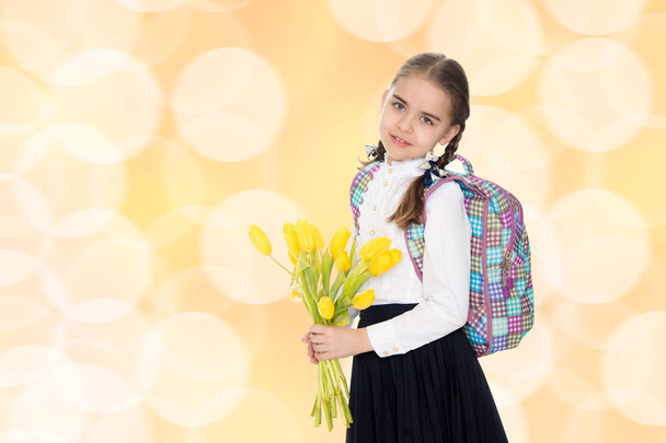 A schoolgirl with a bouquet of flowers and a backpack on her sho - Photo, Image