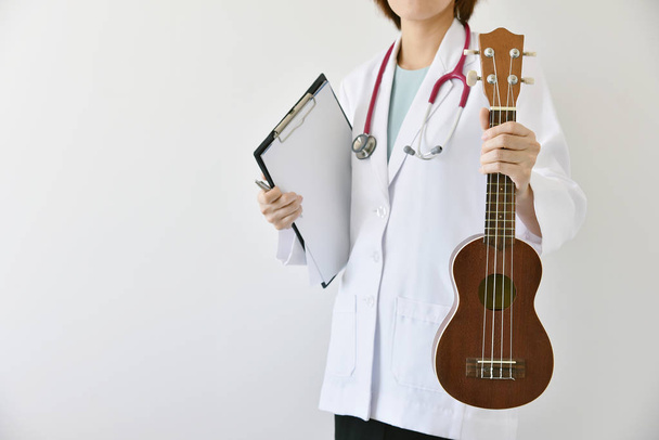 Докторська рука тримає укулеле (музичний інструмент), концепція музичної терапії
. - Фото, зображення