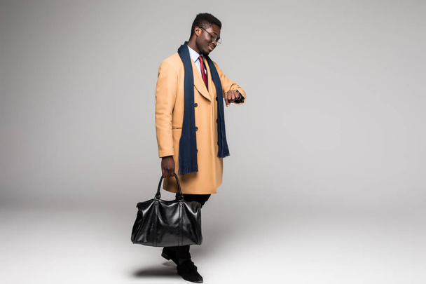 νέοι αφρο αμερικανικό ΕΠΙΤΥΧΗΜΕΝΟ στέλεχος σε παλτό ματιά στο ρολόι ώρας που απομονώνονται σε λευκό φόντο - Φωτογραφία, εικόνα