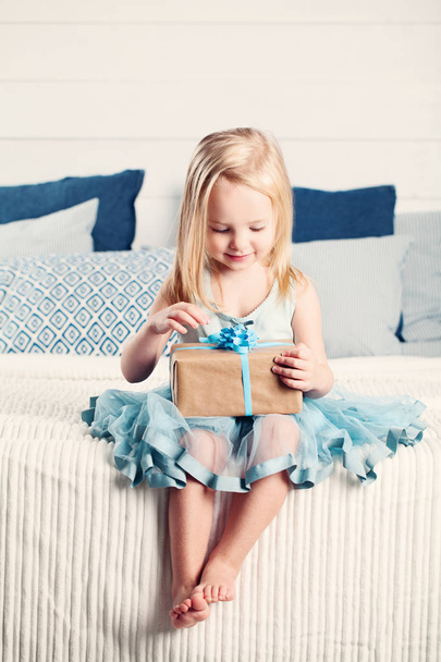 Симпатичная девочка открывает подарок с голубой лентой
 - Фото, изображение