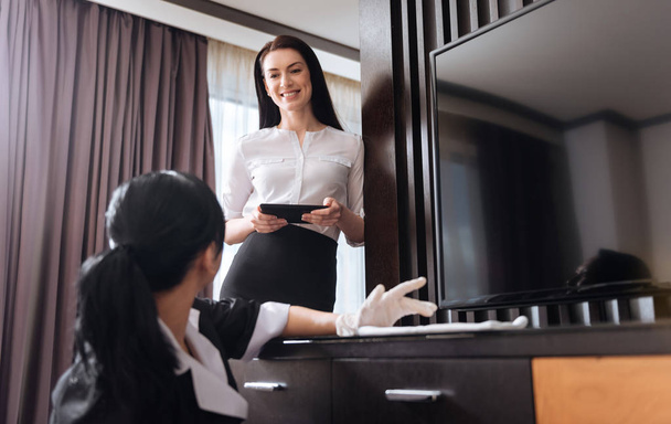 Attractive cheerful woman looking at the hotel maid - Photo, image
