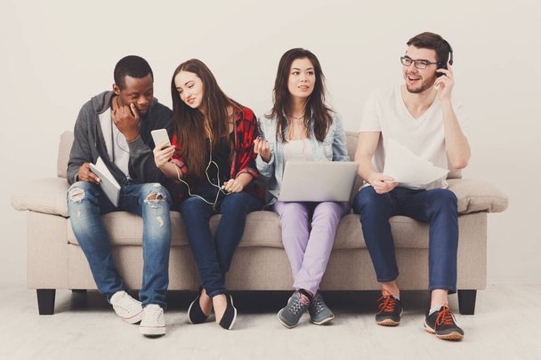 Diverse students using gadgets, sit on sofa - Photo, Image