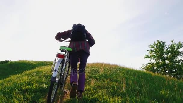 Een moeilijke klim op de heuvel. Een man rijdt een fiets een steile heuvel. De hete zon, veel muggen vliegen. Het overwinnen van moeilijkheden en obstakels - Video