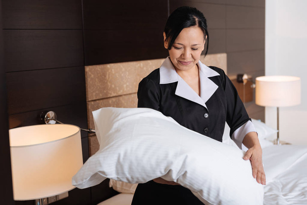 Positive hard working hotel maid looking at the pillow - Photo, Image