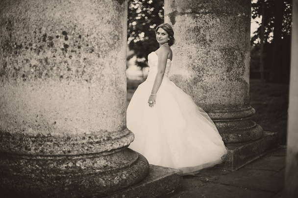 Bride in magnificent dress stands between old pillars - Fotó, kép