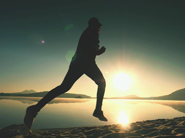 Futó ember strandon. Sportoló fut baseball sapka, jogging srác közben a napkelte homokos strand felett. Ugrás a tengerparton naplementekor, az ember - Fotó, kép
