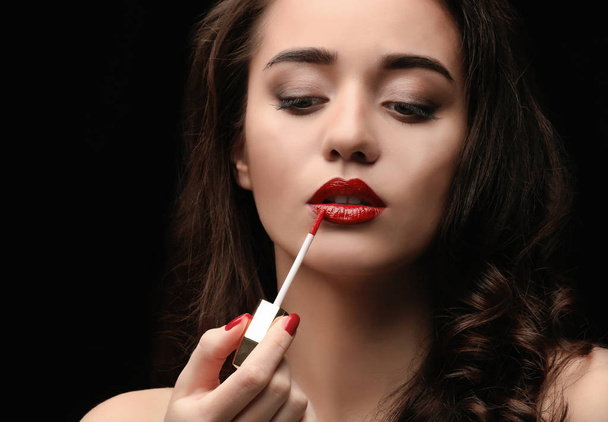 Portrait of beautiful woman applying lipstick on dark background - Photo, Image