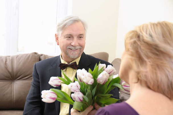 Elderly man and his wife with bouquet of flowers at home - Photo, image