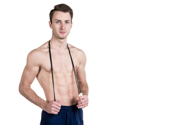 Healthy lifestyle and fitness. Handsome guy sports a physique, with a naked body, with a skipping rope in his hands, isolated on a white background. Horizontal frame - Photo, Image