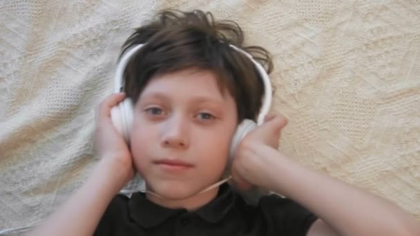 Top view of cute little boy listening to music holding his headphones looking at the camera - Footage, Video