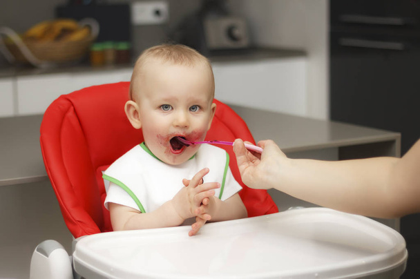 Un niño pequeño come mermelada y cereales, se sienta en una trona
 - Foto, imagen