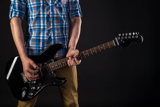 Música y arte. El guitarrista sostiene una guitarra eléctrica en sus manos, sobre un fondo negro aislado. Tocando guitarra. Marco horizontal
 - Foto, imagen