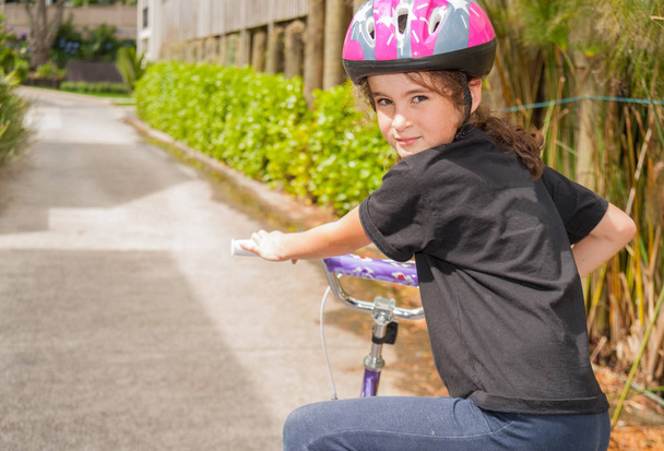 Νεαρό κορίτσι ιππασία ποδήλατο φορώντας κράνος γυρίζει το κεφάλι και το βλέμμα - Φωτογραφία, εικόνα