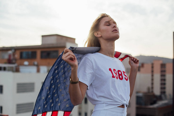 Ξανθό μοντέλο γυναίκα κρατά ψηλά την αμερικανική σημαία - Φωτογραφία, εικόνα