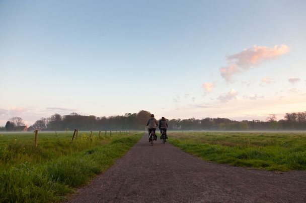 Turistit pyöräilemässä tiellä niityllä sumussa auringonlaskun aikaan
. - Valokuva, kuva