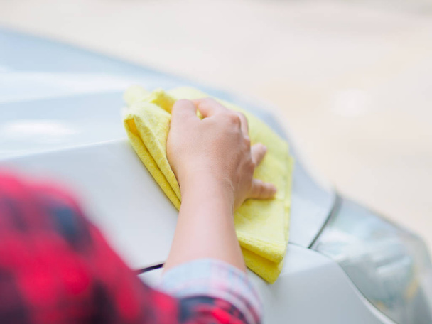 Hand with yellow microfiber cloth cleaning white car. - Zdjęcie, obraz