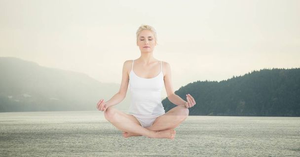 Digital composite of Double exposure of woman meditating over lake - Foto, afbeelding