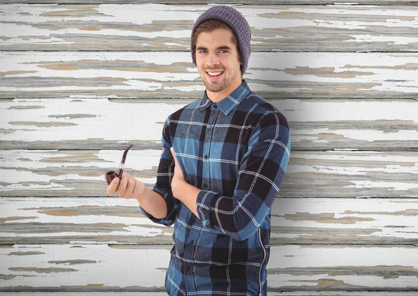 Smiling hipster holding smoking pipe over wooden wall - Foto, imagen