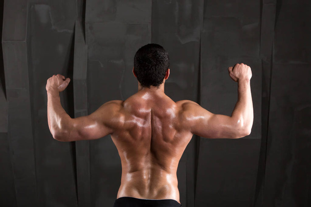 Back of a muscular man on a dark background. Body-builder. - Фото, изображение