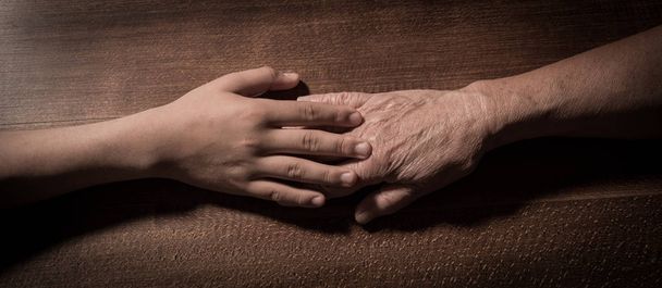 Child hands holding senior woman's hands on brown background - Foto, immagini