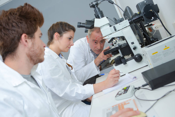 Teacher instructing students on use of microscope - Фото, изображение