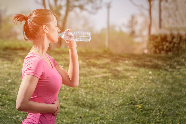 Young sportswoman drinking water during morning jogging  - Photo, Image