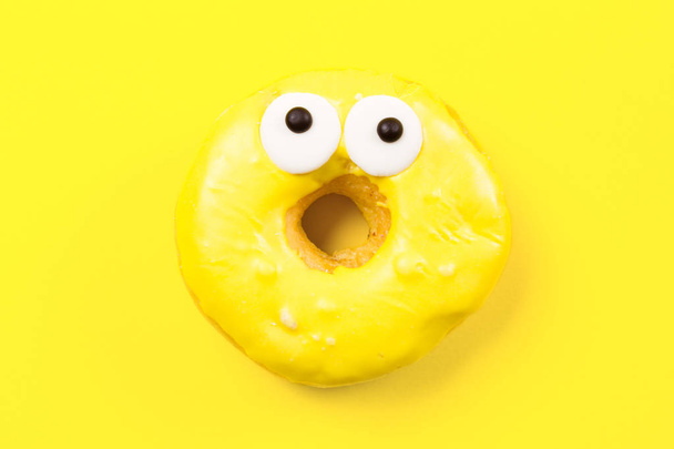 Round donut with eyes on yellow background. Flat lay, top view. - Photo, Image