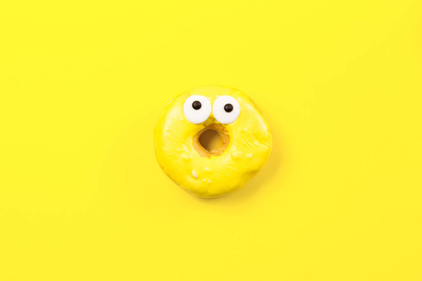 Στρογγυλό donut με μάτια σε κίτρινο φόντο. Επίπεδη lay, κορυφαία προβολή. - Φωτογραφία, εικόνα