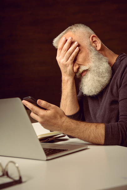 man holding smartphone with facepalm - Photo, Image