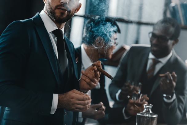 бизнесмен курит сигары с мультикультурным бизнесом команда проводит время позади
 - Фото, изображение